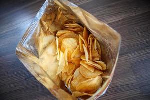 Potato chips in open snack bag close up on table floor photo