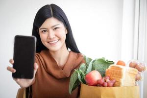 Beautiful Asian woman holding a smartphone, ordering food online. The business concept of food delivery services during the coronavirus. Copy space photo