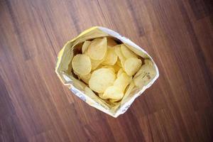 Potato chips in open snack bag close up on table floor photo