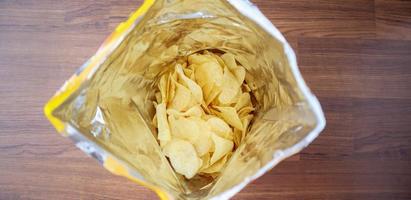 Potato chips in open snack bag close up on table floor photo