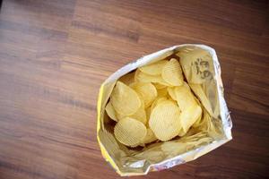 Potato chips in open snack bag close up on table floor photo