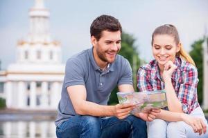 Choosing the place to go. Happy young tourist couple sitting near beautiful building and examining map together photo