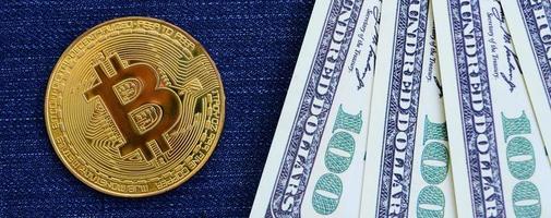 Golden Bitcoin and dollar bills lies on a blue jeans fabric. New virtual money. New crypto currency in the form of the coins photo