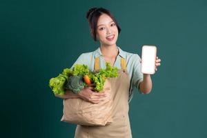 Asian girl portrait holding a bag of vegetables on a green background photo