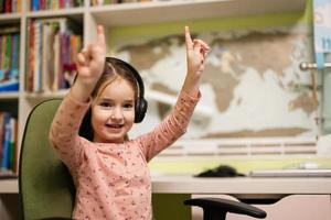 Young girl wearing headphones, enjoys her remote education. Distant studying, homeschooling. Show fingers up. photo