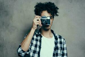 photographer in a plaid shirt with a camera in his hand on a gray background in a hobby studio room photo