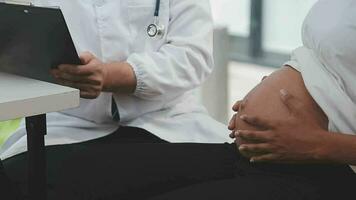 Prenatal health care. Close up of young pregnant woman visiting doctor at antenatal clinic. Medic gynecologist examine fetal heartbeat rate moving stethoscope by naked baby bump of expectant mother video