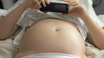 Pregnant woman with bare belly resting at home and using cellphone video