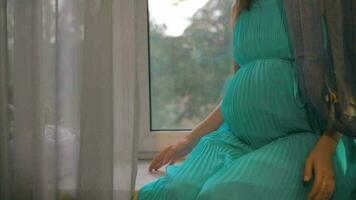 Pregnant woman sitting on windowsill and embracing belly video