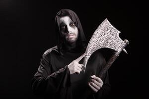 Dangerous scary man dressed up like grim reaper with an axe over black background. photo