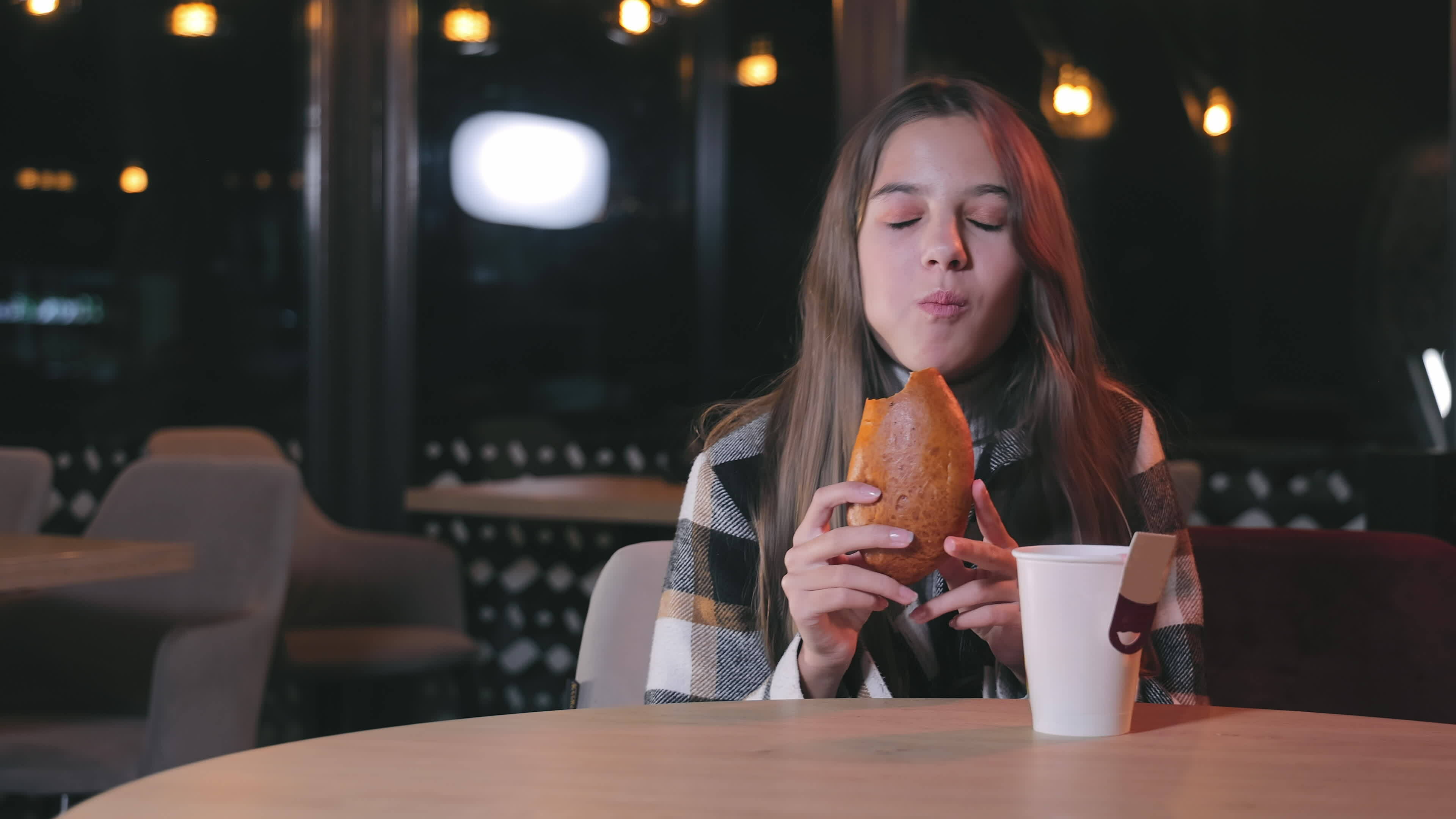 A teenage girl is eating a bun. A girl in a cafe eats a bun in the ...