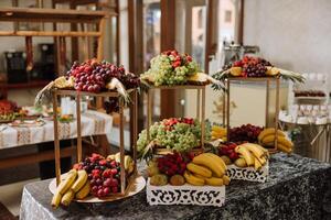 A banquet table full of fruits and berries, an assortment of sweets. Bananas, grapes, pineapples. Fruit compositions for the holiday. photo