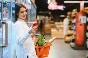 Smiling young woman using mobile phone while shopping in shopping store photo