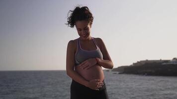 a pregnant woman standing on the beach with her hands on her belly video