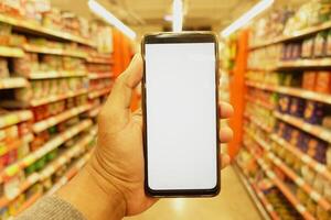 hand holding mobile phone with white screen while shopping at supermarket. photo