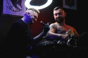 tattoo artist demonstrates the process of getting black tattoo with paint. Master works in black sterile gloves photo