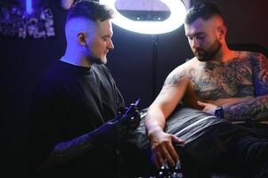 tattoo artist demonstrates the process of getting black tattoo with paint. Master works in black sterile gloves photo