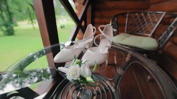 The bride's shoes and the groom's boutonniere lie on a glass table. Accessories for the wedding day video