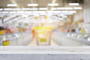 Wooden board empty table in front of of supermarket shelves. Perspective white wood over blur in supermarket photo