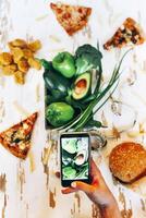 Unrecognizable woman shooting healthy vegetables near junk food photo