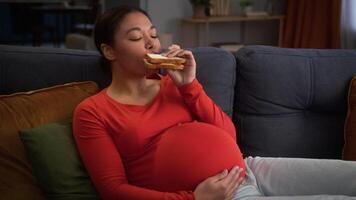 African American girl pregnant woman mother female lady pregnancy child anticipation at home couch sofa waiting baby mom mommy eating sandwich bread eat nutrition food delivery hungry health medicine video