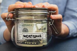 Unrecognizable woman holding Saving Money In Glass Jar filled with Dollars banknotes. MORTGAGE transcription in front of jar. Managing personal finances extra income for future insecurity background photo