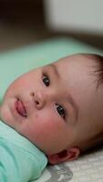 Lovely boy lying peacefully on the bed shows tongue and turns his head away. Little baby resting indoors. Close up. Blurred backdrop. Vertical video