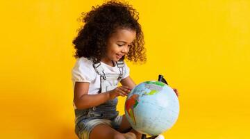 Cute little girl looking at earth globe over yellow studio background photo