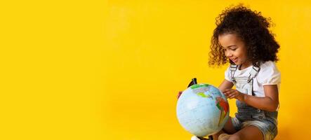 Early education. Little girl pointing to world globe, yellow background, copy space photo