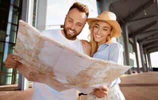 Young couple looking at map after arriving to new travel destination, standing near airport building photo