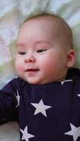 Smiling beautiful toddler being active on the bed. Top view on a nice cute cheerful baby on white backdrop. Vertical video