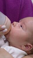 Mother is holding a child in her arms and feeding a baby from a bottle. Baby eating milk and falling asleep gradually. Close up. Vertical video