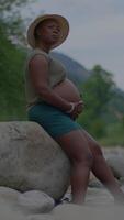 A serene pregnant woman enjoying the beauty of nature by the river amidst lush greenery video