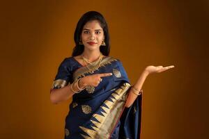 Portrait of Indian traditional young woman or girl presenting something, showing copy space on her palm on a brown background photo