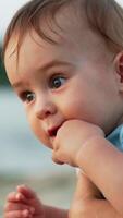 Little baby boy with fingers in his mouth. Mother holding a cute child in hands in nature. Close up. Blurred backdrop. Vertical video