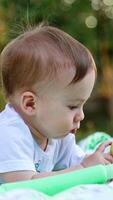 Having rest in the summer garden. Adorable baby boy lies on the belly looking attentively at the apple. Blurred backdrop. Vertical video