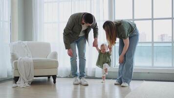 Baby development. Little infant girl making first steps at home. Happy mother father looking at toddler child walking in living room. Happy family at home. Mom dad supporting baby first steps video