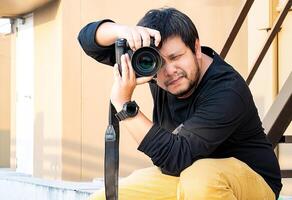 Asian Professional Camera man looks in to camera viewfinder and focus on the view for take a photo at rooftop outdoor field.