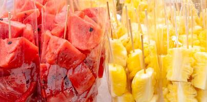 Full frame of red watermelon and yellow pineapple in pieces or slices in transparent plastic bag on sale at street food stall photo