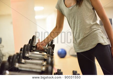 Gym woman strength training lifting dumbbell weights getting ready for exercise workout. Female fitness girl exercising indoor in fitness center. Beautiful fit mixed race Asian Caucasian model.