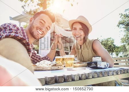 Handsome couple taking selfie with mobile smart phone camera - Young fashion tourist making photo souvenir while eating meal at bar street food restaurant - Vacation and love concept - Warm filter