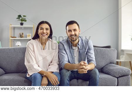 Portrait Of A Happy, Cheerful Young Married Couple Sitting On The Couch At Home