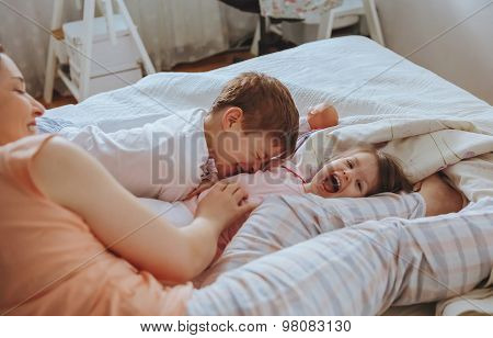 Relaxed mother and sons playing over the bed