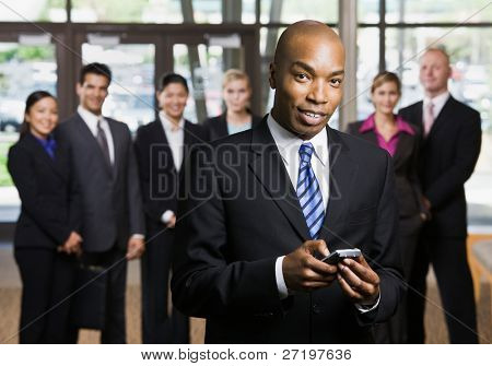 African businessman using cell phone in front of co-workers