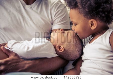 Beautiful young Afro American family spending time together. Little baby is sleeping in dad's arms while her sister is kissing her