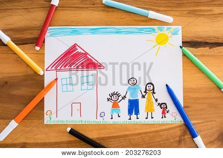 Top view of colored drawing of happy family holding hands together. Little child painted his family on paper. High angle view of painting and markers on table. Concept of unity and love.