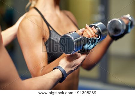 fitness, sport, bodybuilding and weightlifting concept - close up of young woman and personal trainer with dumbbells flexing muscles in gym