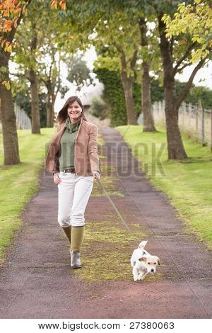 Woman Taking Dog For Walk Outdoors In Autumn Park