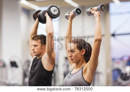 sport, fitness, lifestyle and people concept - smiling man and woman with dumbbells flexing muscles in gym