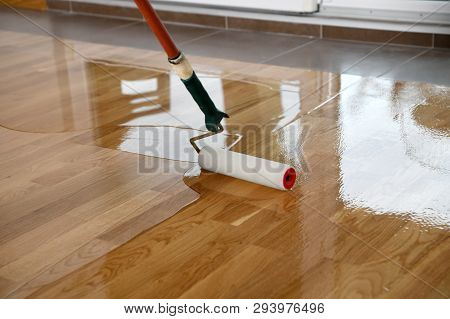 Lacquering Wood Floors. Worker Uses A Roller To Coating Floors. Varnishing Lacquering Parquet Floor 